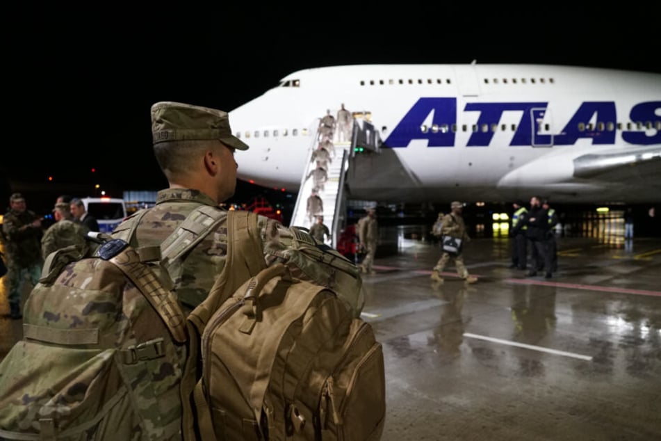 Ein US-Soldat steht mit seinem Gepäck vor dem Flugzeug, während seine Kameraden noch aussteigen.
