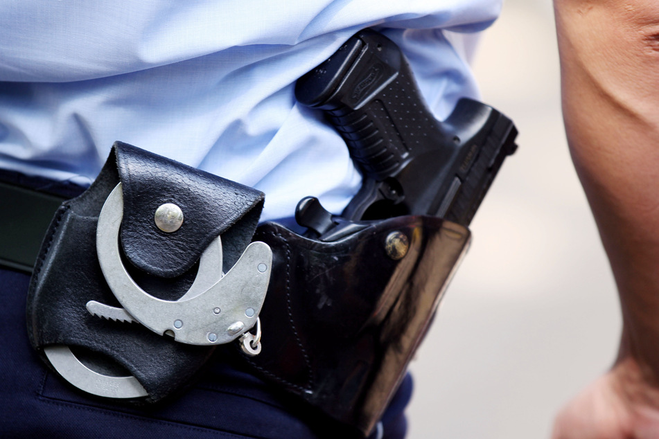 Ein Polizist wartet mit Handschellen und Pistole am Gürtel auf einen Einsatz. (Symbolbild)