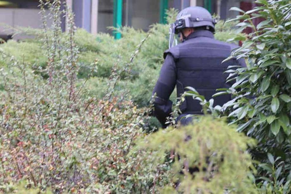 Ein Polizist in Schutzanzug durchsucht das Gebüsch vor dem Haus der Presse.