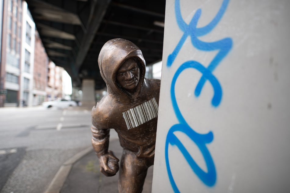 Eine Bronzestatue, die einen Mann mit Kapuzenpulli darstellt, der eine Spraydose in der Hand hält, steht am Pfeiler des U-Bahn-Viadukts am Rödingsmarkt.