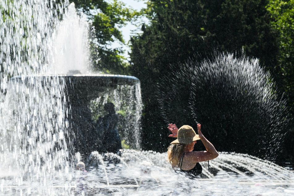 Eine Frau kühlt sich am Albertplatz an den Wasserfontänen der Brunnen "Stilles Wasser" und "Stürmische Wogen" ab.