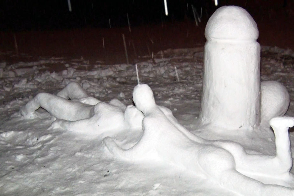 Neben dem Penis vergnügt sich ein Pärchen im Schnee.