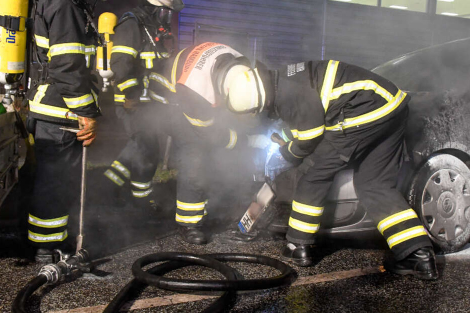 Feuerwehrleute untersuchen ein ausgebranntes Fahrzeug.