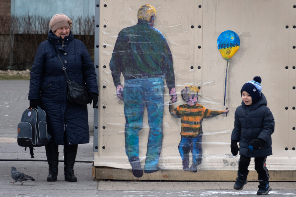 Ein Kind mit Oma neben dem Kunstwerk des berühmten Straßenkünstlers TvBoy. Auf dem Ballon mit den Farben der ukrainischen Flagge steht "Frieden".
