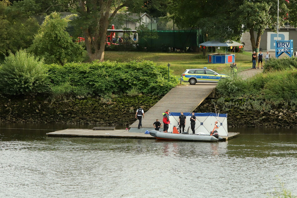 Einsatzkräfte stehen neben dem Sichtschutz am Ufer der Weser.