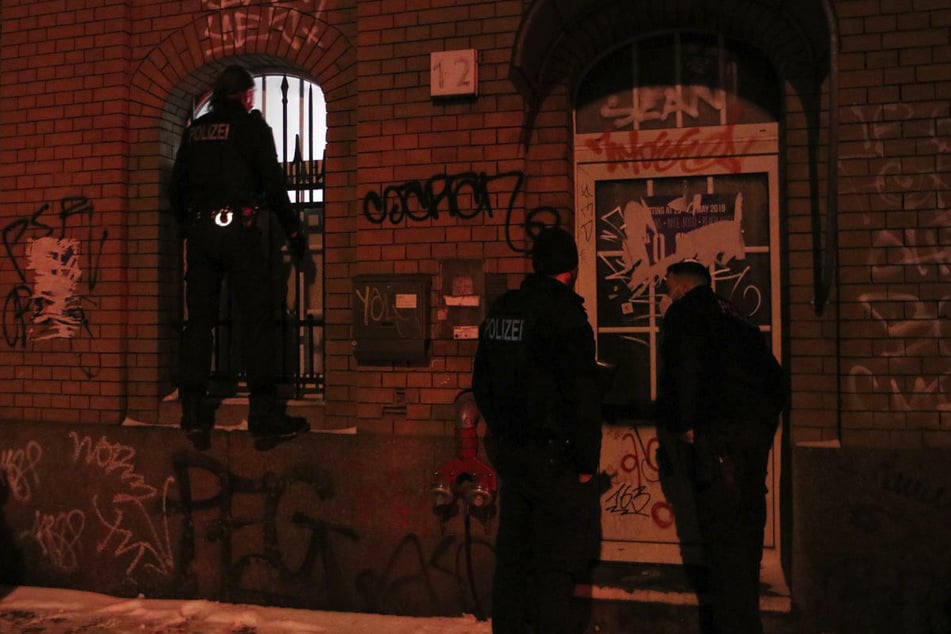 Ein Polizeibeamter versucht durch ein Fenster des Clubs einen Blick auf die Vorgänge im Inneren zu erhaschen, während zwei Kollegen an der Tür warten.