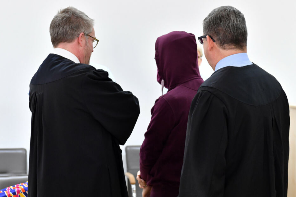 Der Angeklagte mit Handfesseln steht vor Verhandlungsbeginn als mutmaßlicher Mörder eines chinesischen Studenten zwischen seinen Verteidigern im Sitzungssaal des Landgerichts.