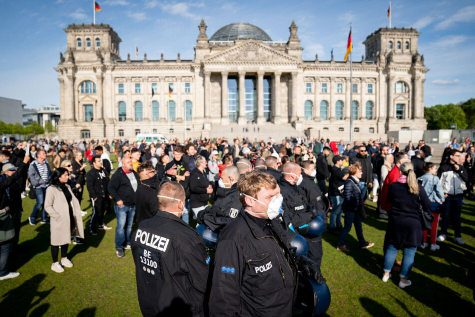 Polizeibeamte mit Mund-Nasen-Schutz stehen in einer Menschenmenge auf der Reichstagswiese vor dem Reichstagsgebäude.