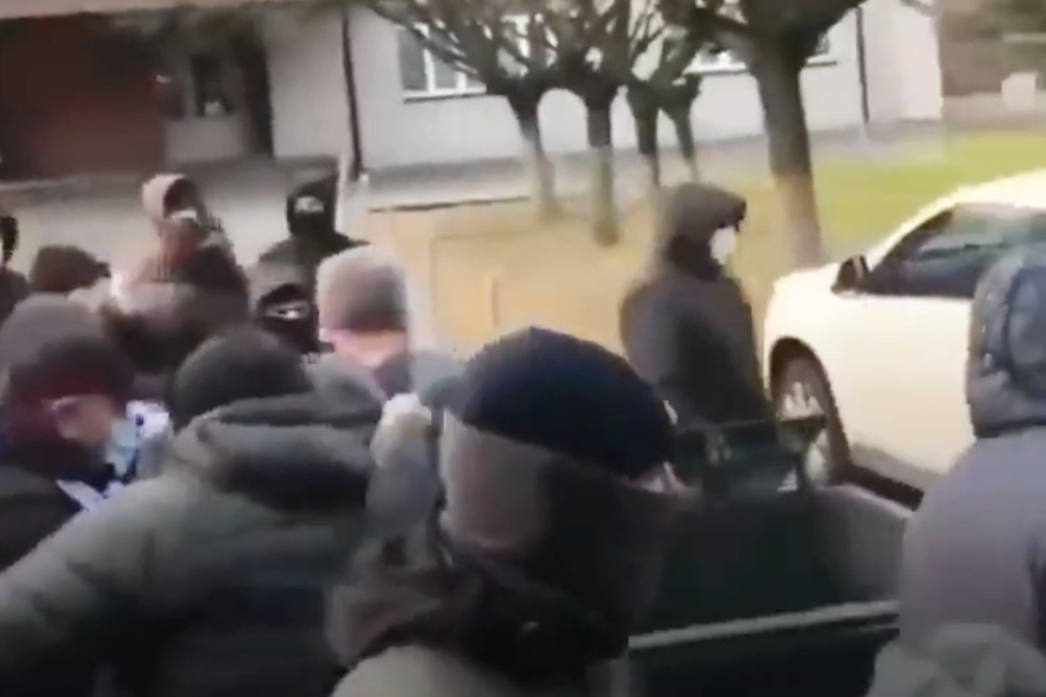 Ein Ultra packt den Präsidenten Oleksandr Ovrachenko (4.v.r.), der in einer Mülltonne durch die Straßen geschoben wird, heftig am Kragen.