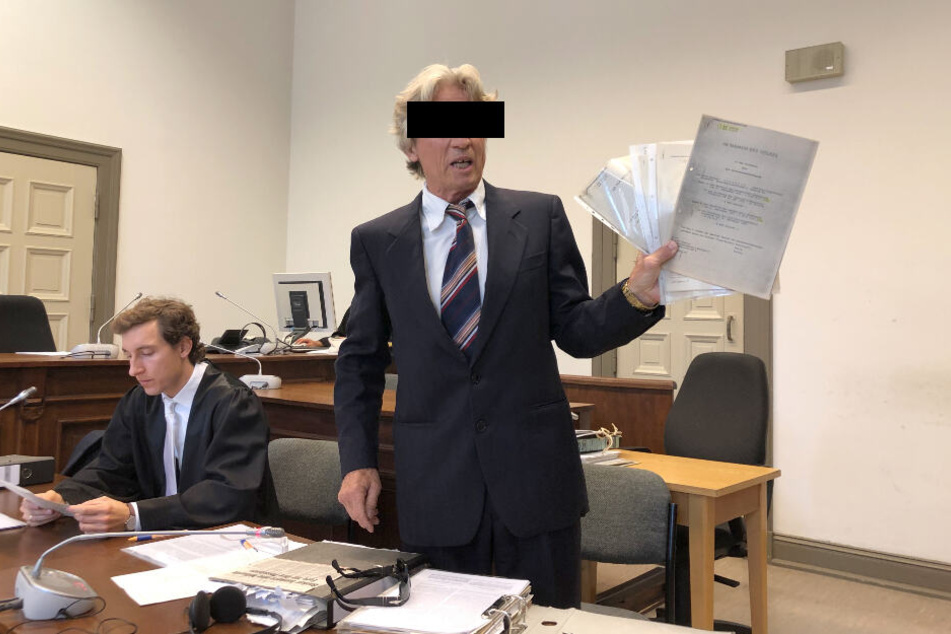 Der Anklagte hält einen Stapel von Papieren in seinen Händen.