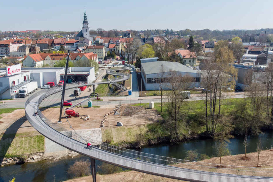 Bauarbeiter sind an einer geschwungenen Schrägseilbrücke mit den letzten Vorbereitungen für die Landesgartenschau in Frankenberg/Sachsen beschäftigt.