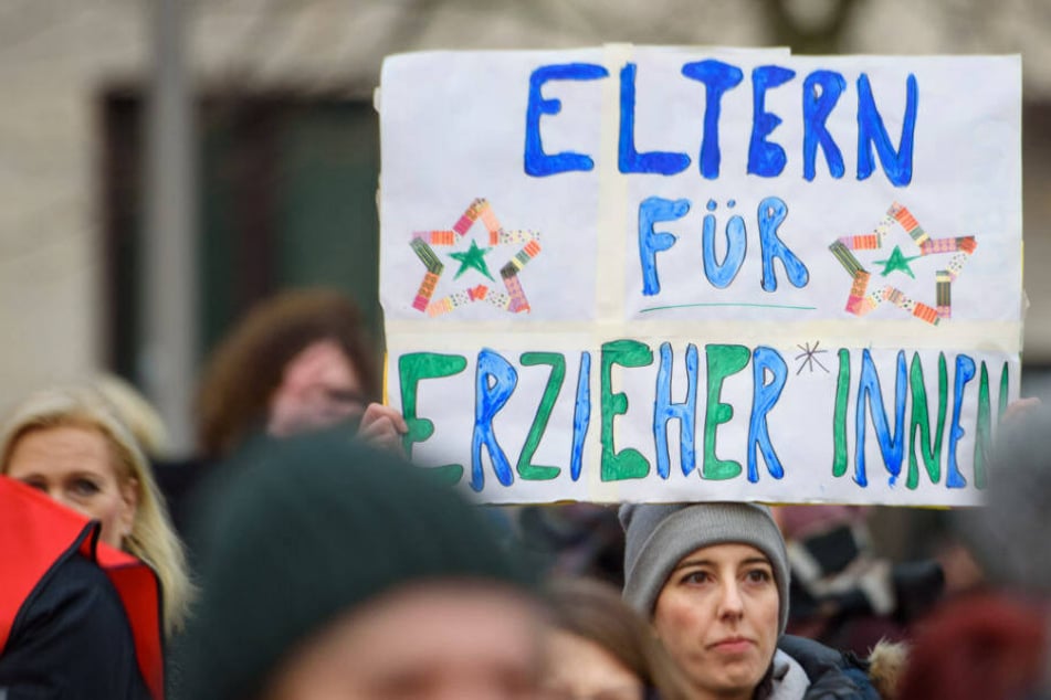 ErzieherInnen und LehrerInnen und weitere Teilnehmer stehen während eines Warnstreiks mit u.a. mit einem Schild "Eltern für Erzieher*innen" auf dem Dorothee-Schlegel-Platz, um für faire Löhne und bessere Arbeitsbedingungen zu demonstrieren.