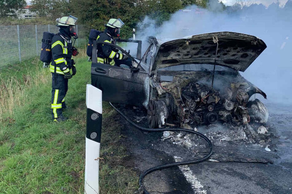 Feuerwehrleute stehen neben dem qualmenden Fahrzeug.