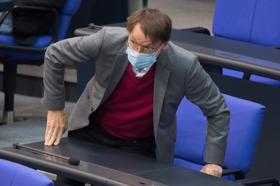Karl Lauterbach (SPD) kommt zu einer Sitzung des Deutschen Bundestags und nimmt auf einem Stuhl Platz.