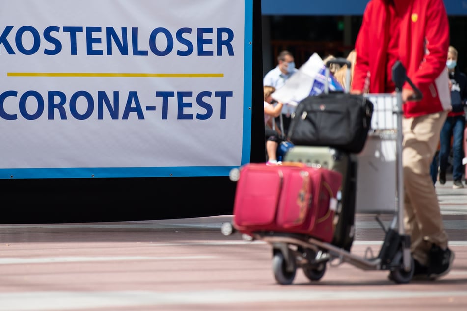 Flugreisende gehen am Flughafen München an einem Schild mit der Aufschrift "Kostenloser Corona-Test" entlang.