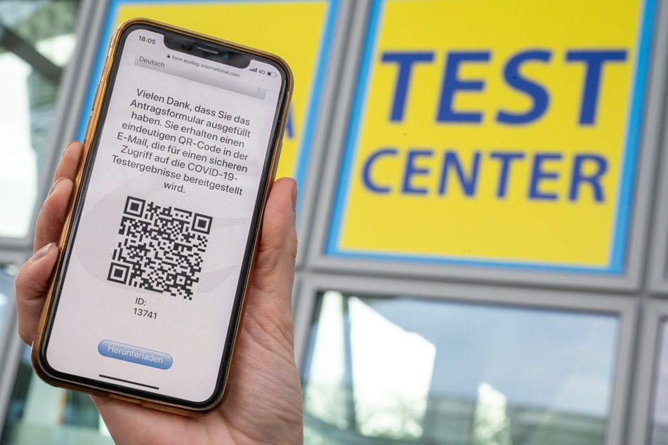 Eine Frau hält ihr Smartphone in die Kamera, mit dem sie sich zuvor am Flughafen für den Coronatest angemeldet hat.