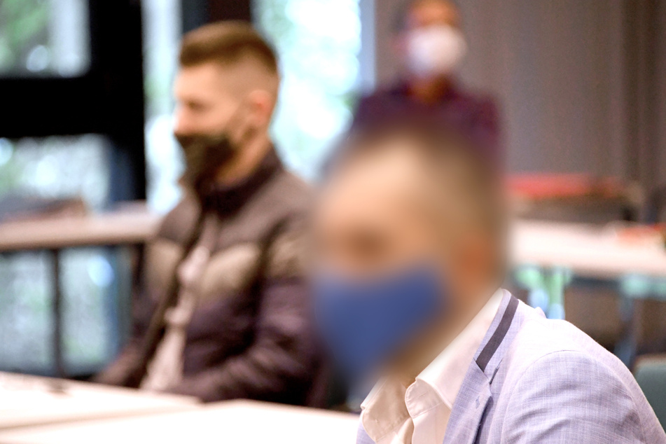 Zwei der Angeklagten sitzen beim Auftakt im Prozess gegen drei Männer im Gerichtssaal.
