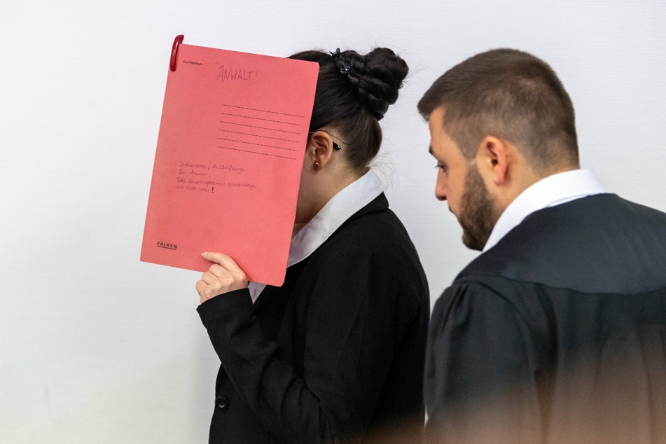 Die Angeklagte Jennifer W., die sich der Terrormiliz Islamischer Staat (IS) im Irak angeschlossen haben soll, hält sich beim Betreten des Gerichtssaals einen roten Aktendeckel vors Gesicht. Rechts steht ihr Anwalt Ali Aydin.