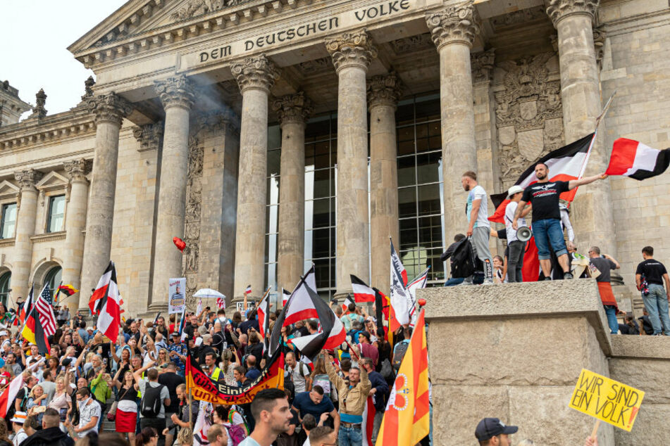 Teilnehmer einer Kundgebung gegen die Corona-Maßnahmen stehen auf den Stufen zum Reichstagsgebäude, zahlreiche Reichsflaggen sind dabei zu sehen.