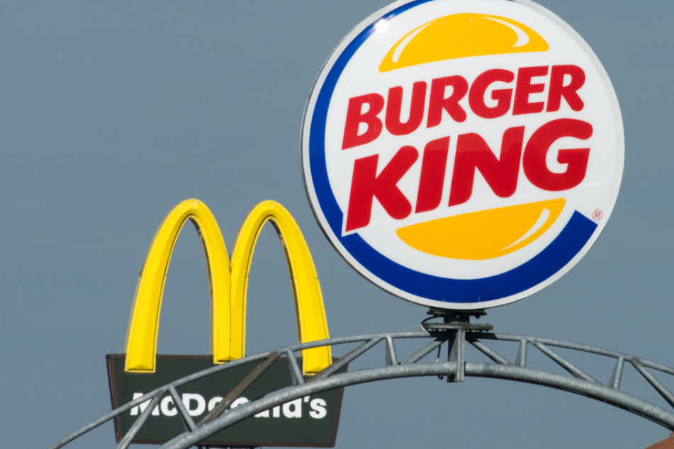 Schilder mit den Logos der Fastfood-Ketten McDonald's und Burger King stehen auf einem Autobahn-Rasthof nahe beieinander.