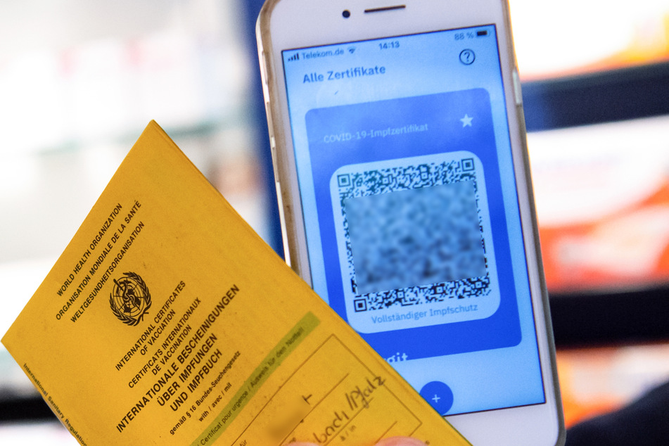 Bayern, München: Ein Apotheker hält einen Impfpass und einen digitalen Impfnachweis in den Händen.