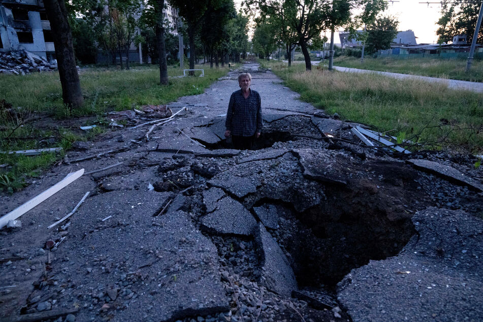 Ein Mann steht in einem Krater, um zu zeigen, wie tief der Krater ist, der durch eine Granate bei einem russischen Angriff im Stadtteil Saltiwka in Charkiw entstanden ist.