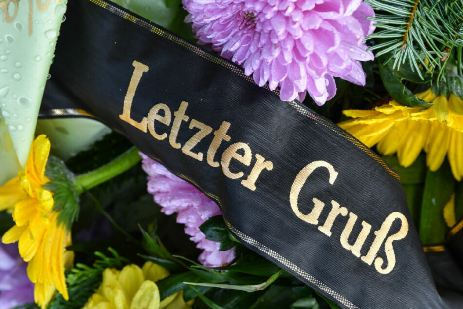 Eine Trauerschleife mit der Aufschrift "Letzter Gruß" auf einem Grab. Aufgrund der Corona-Pandemie werden viele Trauerfeiern ins Freie verlegt. (Symbolfoto)
