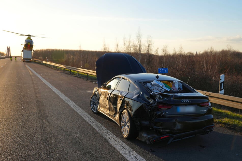 Die Fahrerseite des Audi ist schwer beschädigt. Im Hintergrund ist der Rettungshubschrauber zu sehen.