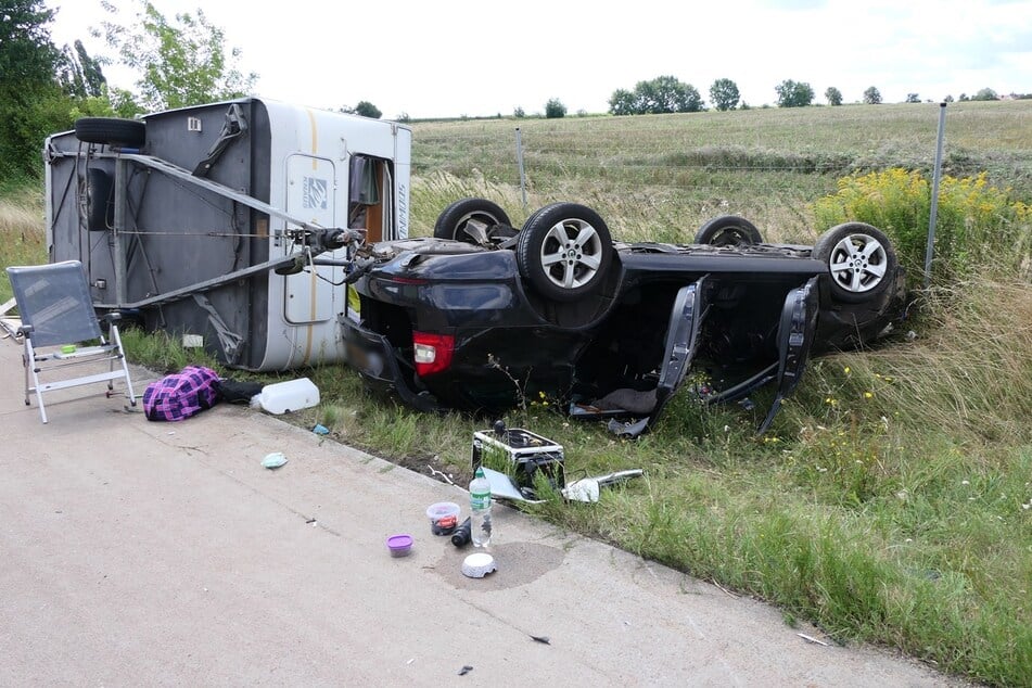 Nach einem Unfall am Samstag auf der A14 nahe Leipzig liegt ein Anhänger auf der Seite und ein Auto auf dem Dach.