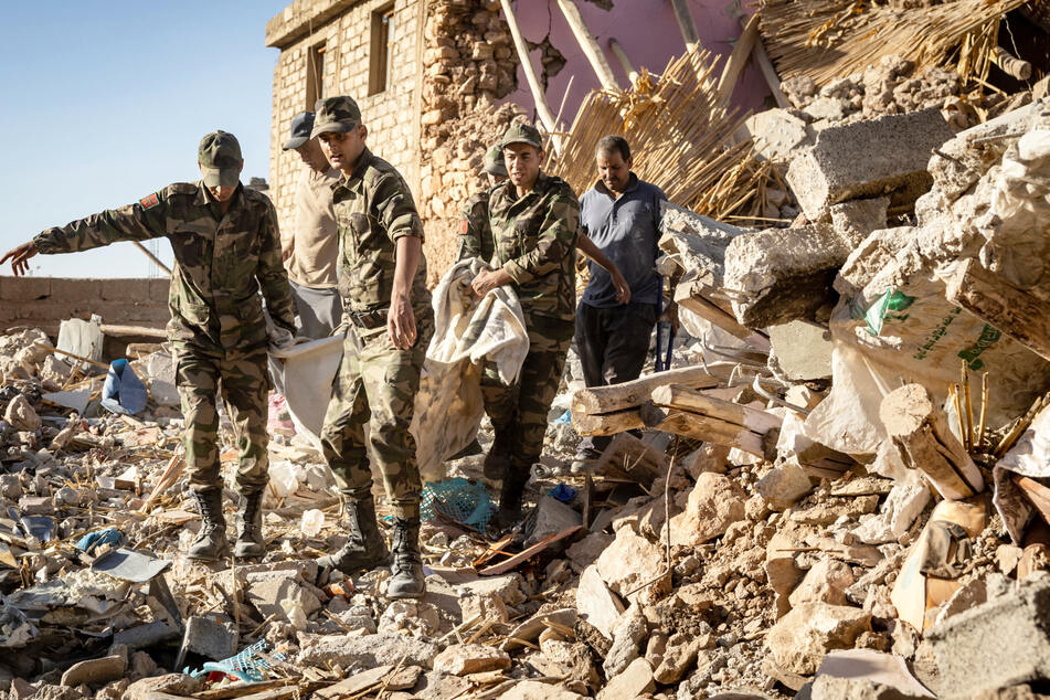 Soldaten der marokkanischen Armee tragen einen leblosen Körper aus einem zerstörten Haus.