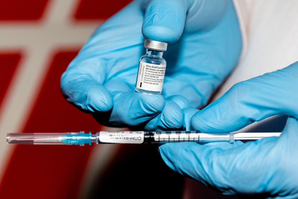 Ein Arzt hält eine Ampulle mit Corona-Impfstoff und eine Spritze in seinen Händen.