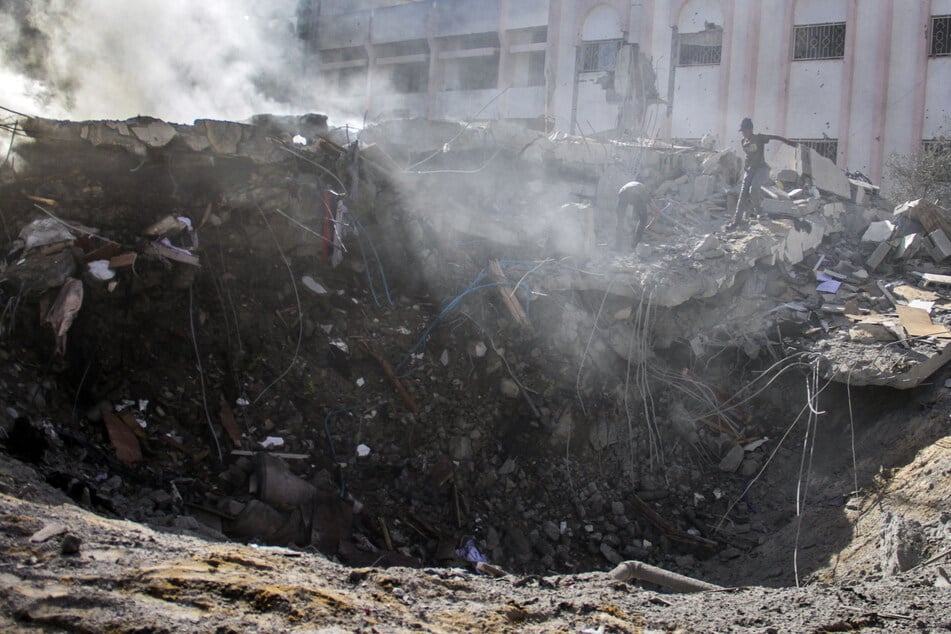 Ein riesiger Bombenkrater raucht, während Palästinenser ihre zerstörten Häuser inspizieren, nachdem israelische Flugzeuge einen ganzen Wohnblock im Viertel Sheikh Radwan im westlichen Gazastreifen ins Visier genommen haben.