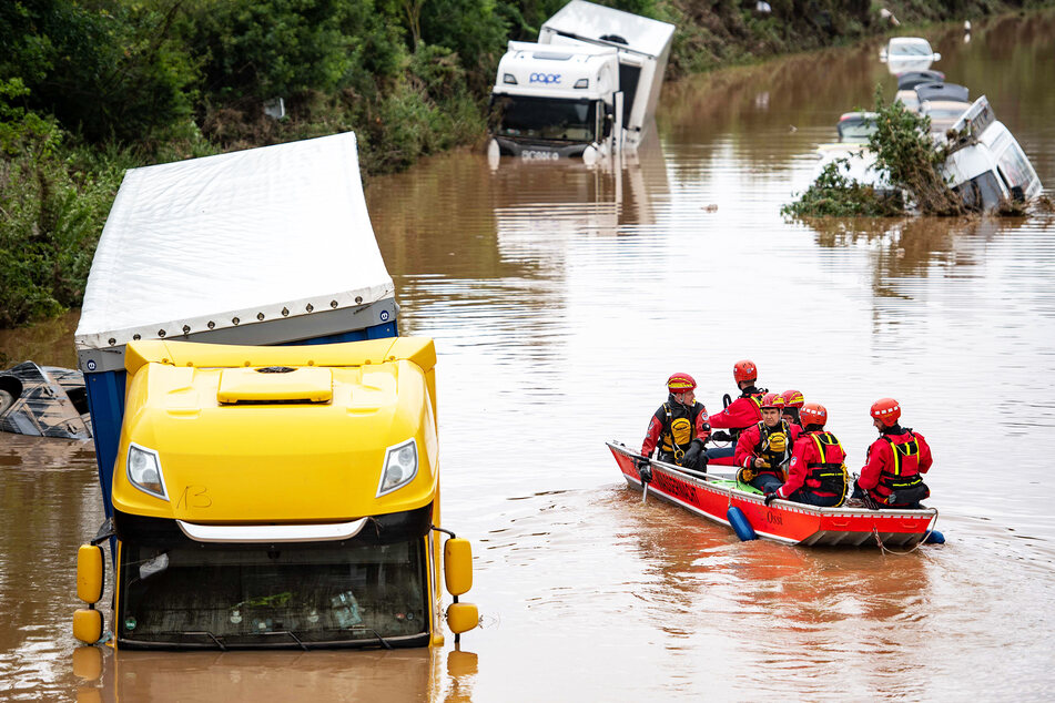 Helfer der Wasserwacht untersuchen von einem Boot aus Lastwagen, die auf einer überfluteten Straße in Erftstadt stehen.