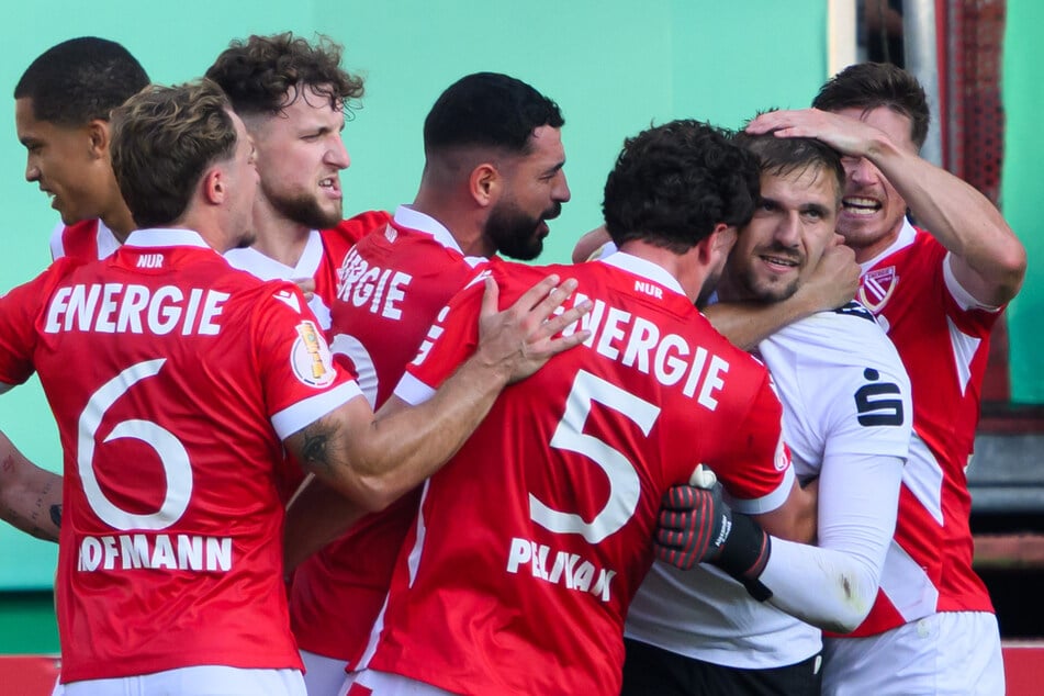 Die Spieler von Energie Cottbus feiern Keeper Alexander Sebald nach dessen gehaltenem Elfmeter.