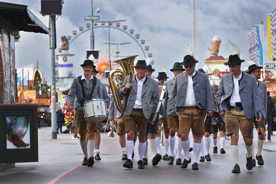 Blasmusiker gehen vor dem Riesenrad über den Festplatz.