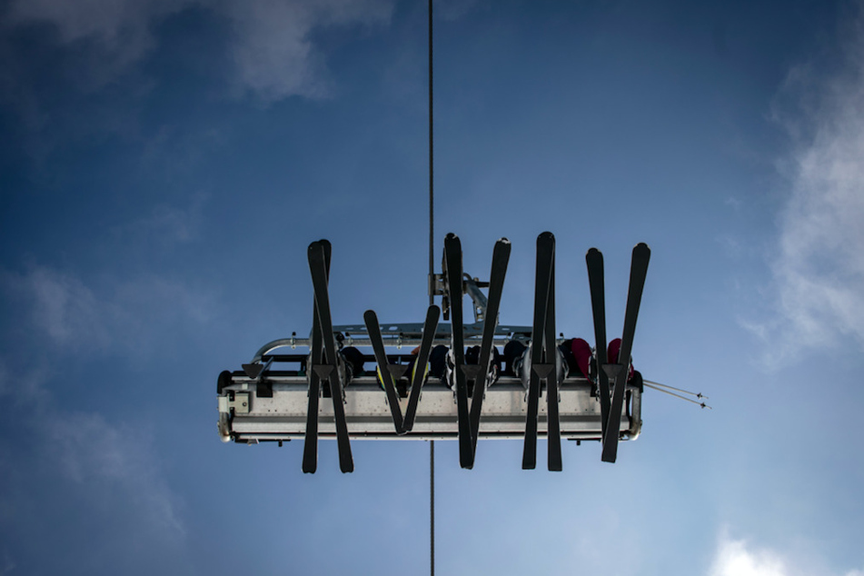 Skier in einem Lift zeichnen sich vor dem blauen Himmel ab.