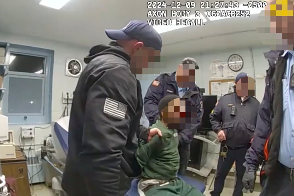 The 43-year-old sits injured on the bed, surrounded by uniformed men - all of them white.