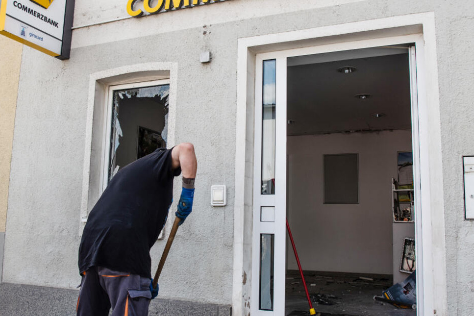Ein Mann kehrt vor einer Bankfiliale der Commerzbank, in welcher am frühen Morgen ein Geldautomat gesprengt wurde, Scherben einer Fensterscheibe zusammen.