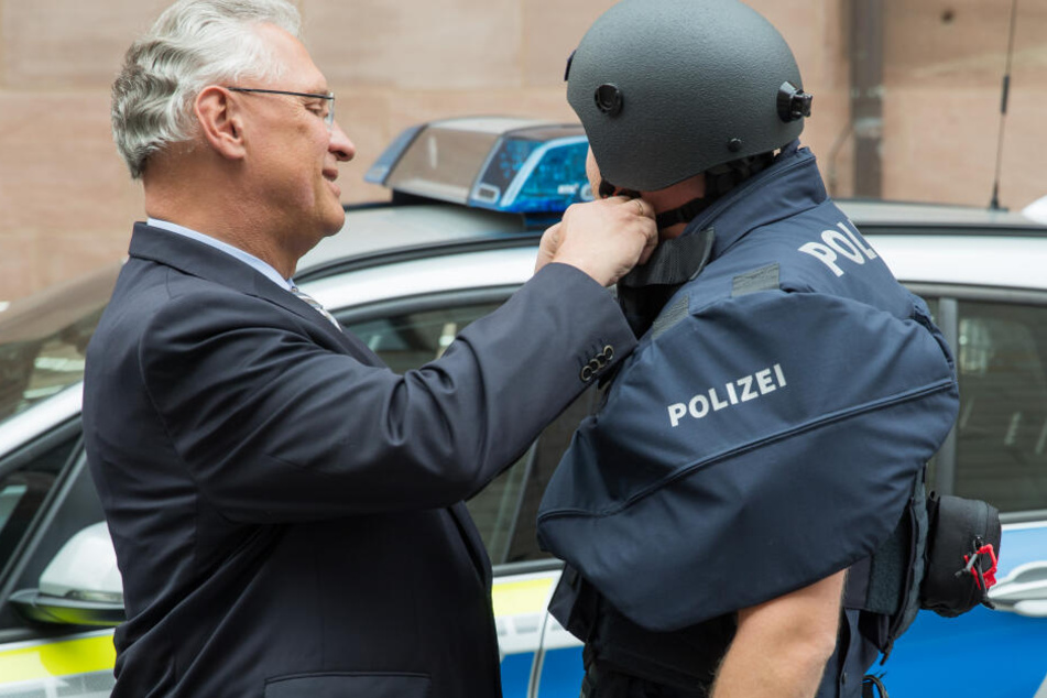 Der bayerische Innenminister Joachim Herrmann (l, CSU) hilft einem Polizisten mit Kugelsicherer Weste der Schutzklasse vier einen neuen ballistischen Schutzhelm zu schließen.