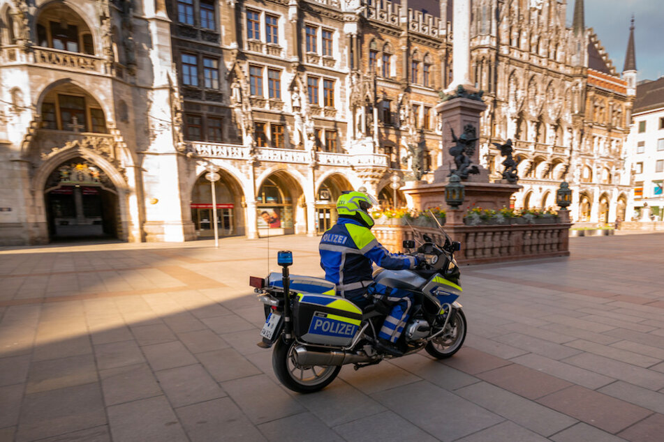 Ein Polizist auf einem Motorrad fährt über den menschenleeren Münchner Marienplatz.