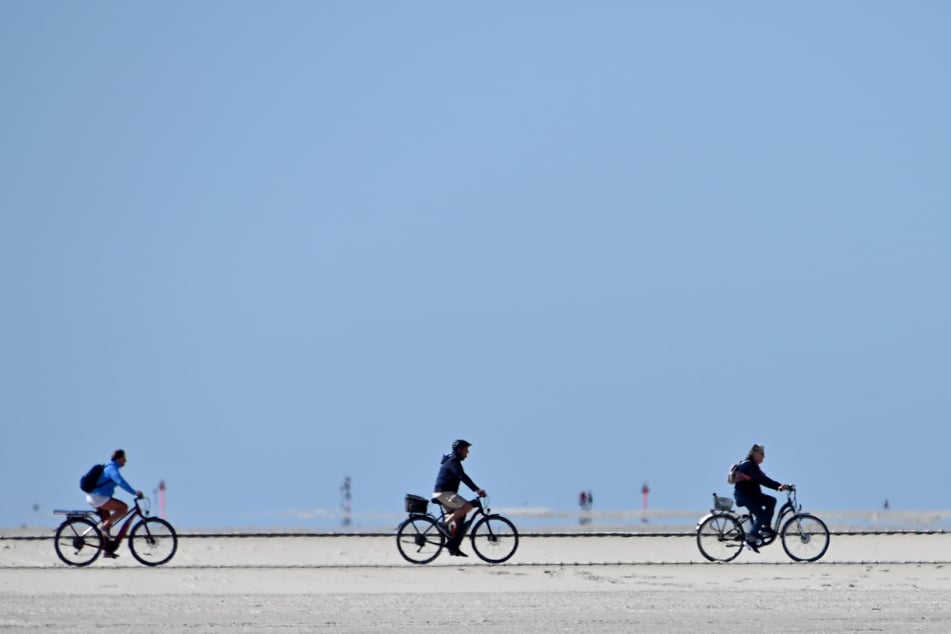 Radfahrer fahren bei blauem Himmel über den Nordseestrand.