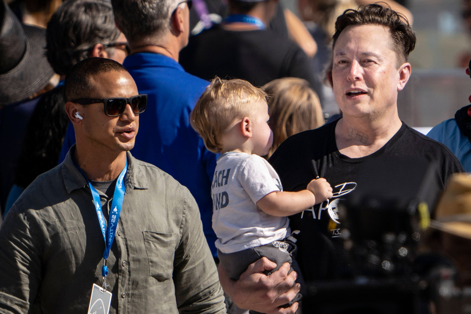 Elon Musk (r.) walks near the terminal as he looks for a good spot to watch the launch of Branson's Virgin Galactic VSS Unity. In his arms is his son X Æ A-Xii, who he shares with singer Grimes.