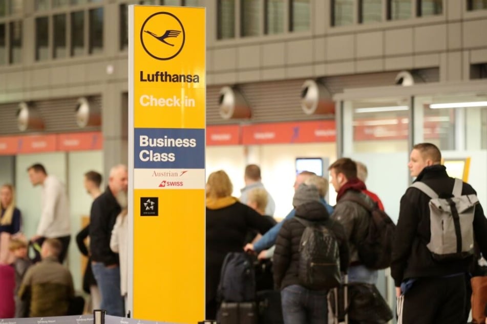 Reisende stehen am Flughafen Hamburg neben einem Lufthansa-Schild.