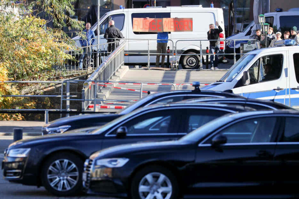Ein Mann hält ein selbstgemaltes Pappschild "Ausgemergelt" hinter einer Polizeiabsperrung und den Dienstwagen der Kanzlerin vor der Hartmannhalle in Chemnitz in die Höhe.