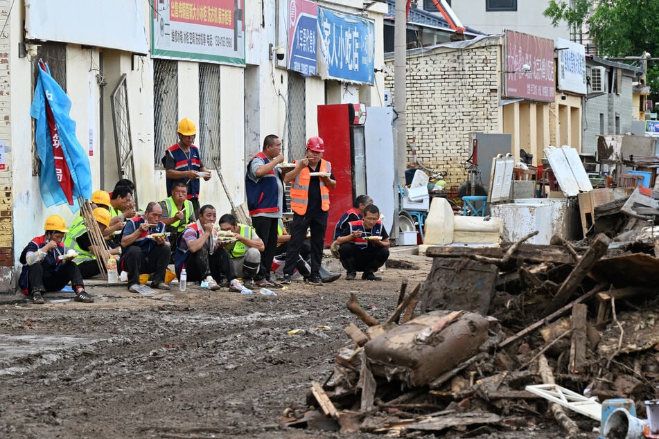 Workers eat their lunch beside a mud-covered road strewn with debris following deadly flooding in Taishitun village, Miyun district, Beijing on August 5, 2025.