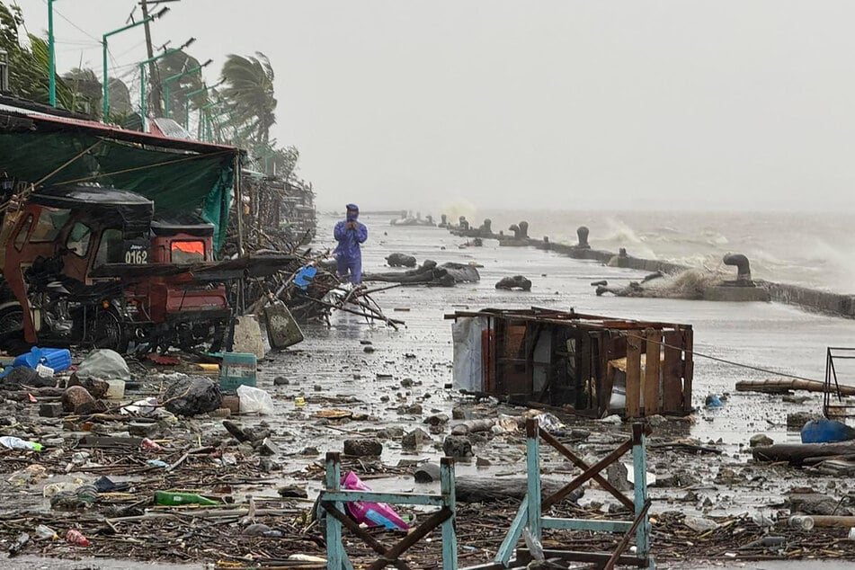 A man stands near debris on a waterfront road amid heavy rain due to weather patterns from Super Typhoon Ragasa in Aparri town, Cagayan province, Philippines, on September 22, 2025.