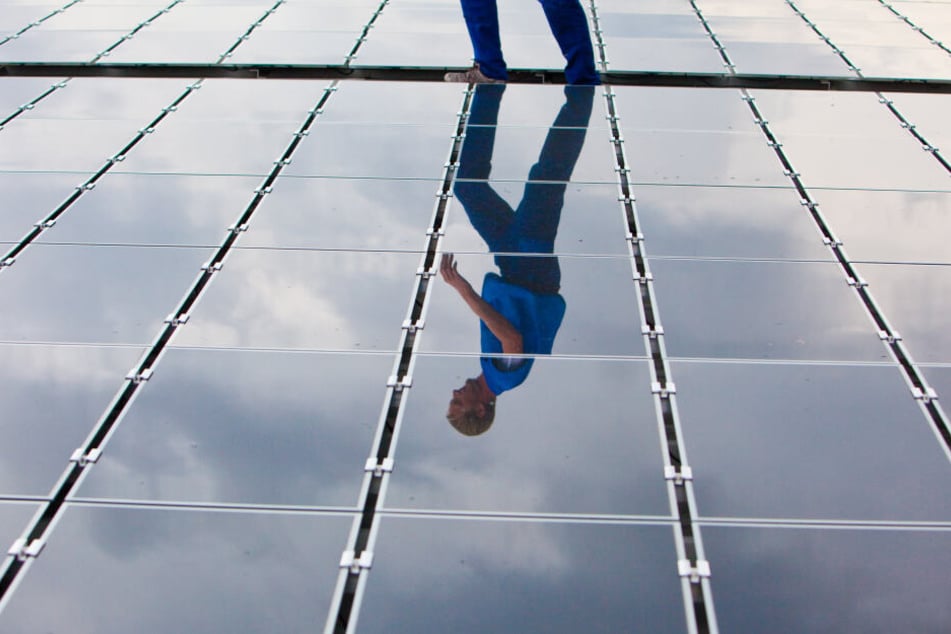 Ein Elektriker läuft für Wartungsarbeiten über ein Dach mit Solarplatten (Symbolbild).