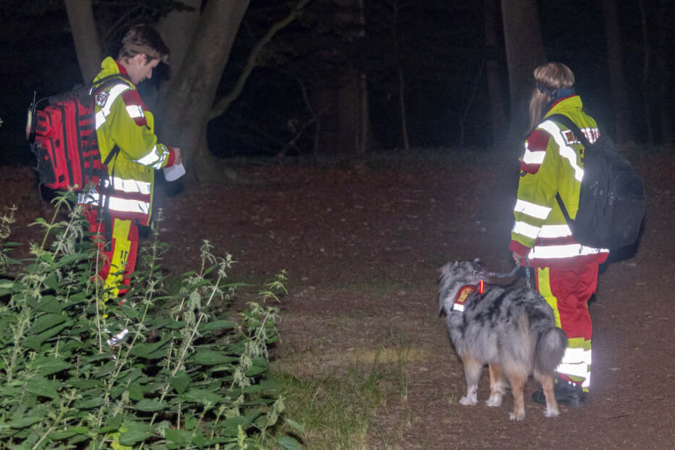 Zwei Einsatzkräfte stehen mit einem Spürhund in der Fischbeker Heide.