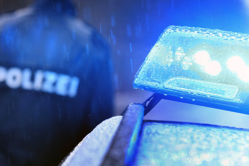 Ein Polizist steht im Regen neben einem Einsatzfahrzeug mit leuchtendem Blaulicht.