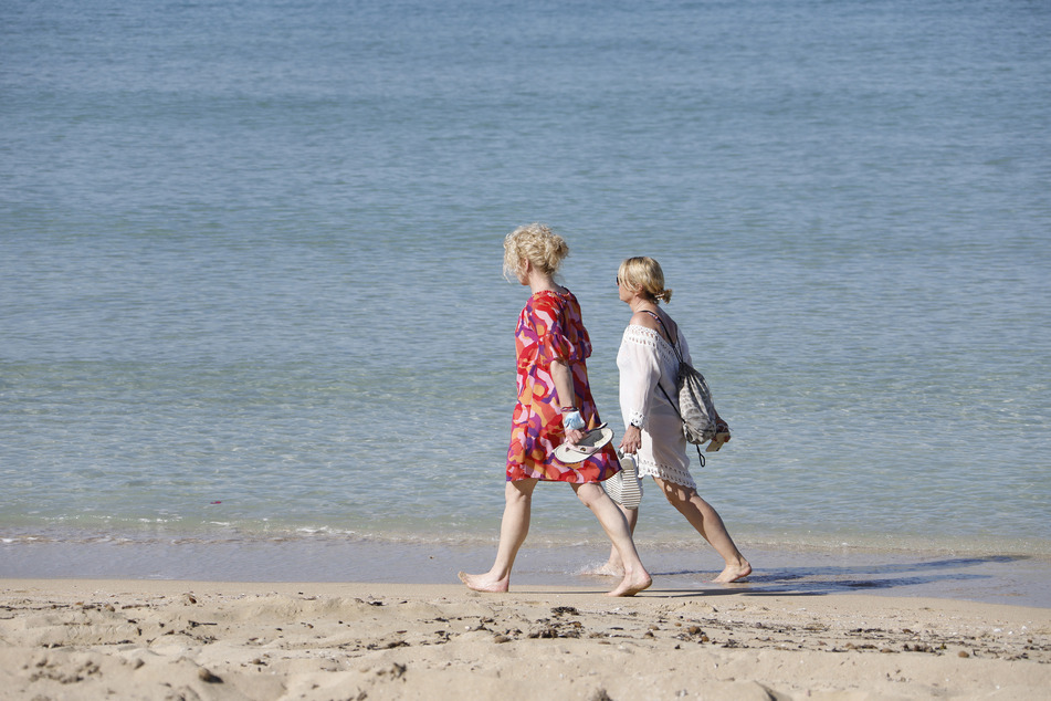 Zwei Frauen gehen am Strand von Arenal am Wasser entlang.